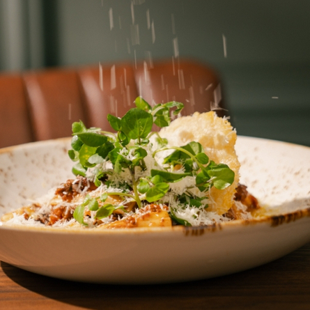 An image showing a bowled Game Ragu Rigatoni dish from the Game Specials menu sat on a wooden table within the interior restaurant seating area at a Chef & Brewer venue.