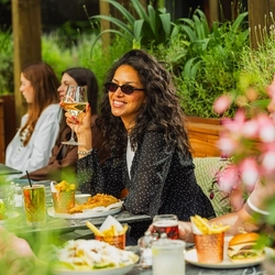A group of people enjoying various dishes from the mains menu and drinks within the exterior beer garden seating area at a Crafted venue.