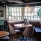 An interior restaurant seating area at The Ship; with wooden beams on the walls and ceiling, and padded bench seating in the large bay window.