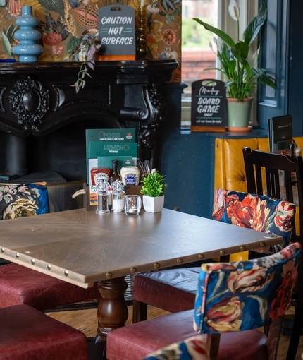 A close up view of a restaurant table in front of the ornate, black fireplace inside The Victoria.