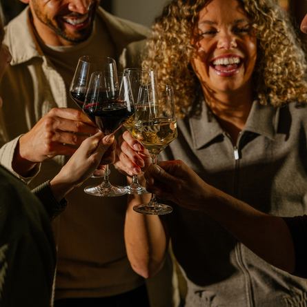 An image of 4 customers enjoying glasses wine and celebrating with a cheers stood within the interior of The Crown.
