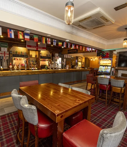 Interior dining area of a pub with a bar, a TV, a fireplace and a gambling machine.