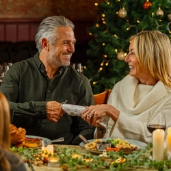 An image of 2 adults pulling a Christmas cracker while enjoying main dishes and drinks within the interior restaurant seating area at a Venture Hotel venue.