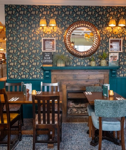 The bar and interior restaurant seating area of The White Lion, with framed artwork on the wall, and a fireplace.