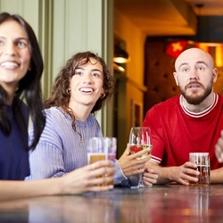 A mixed group of people, sitting at an indoor table reacting to a sporting event.