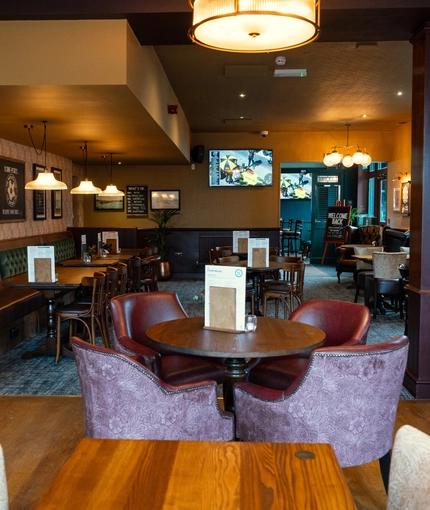 The interior restaurant seating area at The Richmond Arms in Bournemouth, with upholstered chairs and booth seating; and a TV on the wall.