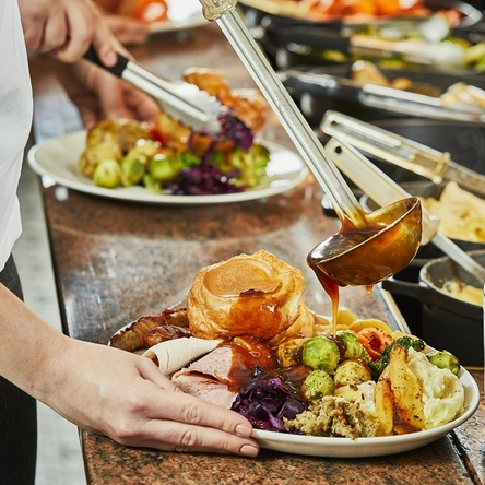 a woman pouring some gravy into a plate of Sunday roast