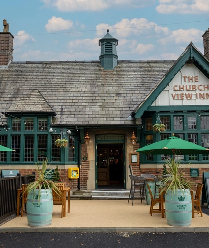 The exterior facade of the venue with hanging baskets, wooden benches and barrel planters at The Church View Inn.