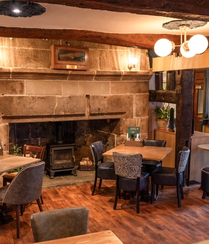 An interior restaurant seating area at The Red Lion, with a large stone fireplace, wooden beams on the ceiling, and a dog treat station.