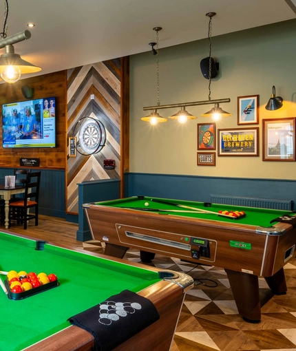The interior pub games area with two pool tables, a dart board and TV's on the wall with the seating area in the background at the Armstrongs.