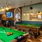 The interior pub games area with two pool tables, a dart board and TV's on the wall with the seating area in the background at the Armstrongs.
