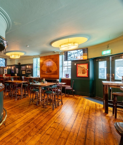 The bar and interior restaurant seating area at the Royal George; with wooden flooring, TVs on the walls, and a large wooden inlay picture of a sailing ship on the wall above the fireplace.