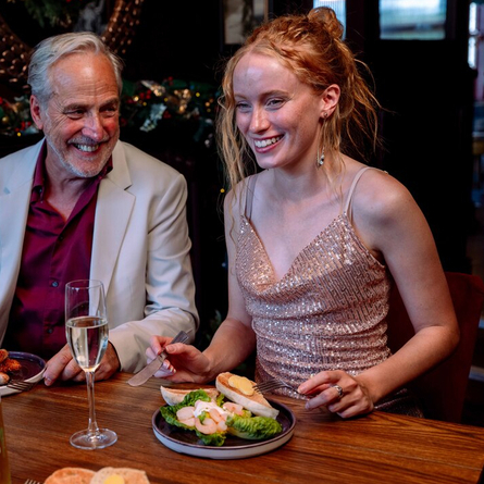 An image showing 2 people sat at a table with other enjoying New Years Eve food and drinks within the interior restaurant seating area at a Community Social venue.