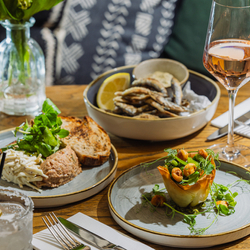 An advertising image showing a selection of starter dishes from the Prix Fixe menu sat on a table within the interior restaurant seating area at The Four Oaks.