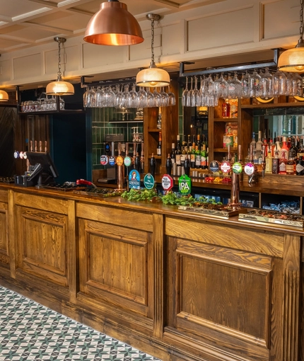 The wood panelled bar inside The White Lion, with wine glasses hanging in racks above the counter.