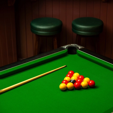 A close up view of the pool table at the Phoenix; with a pool cue and the balls arranged in a triangular shape sitting on the table, and bar stools visible in the background.