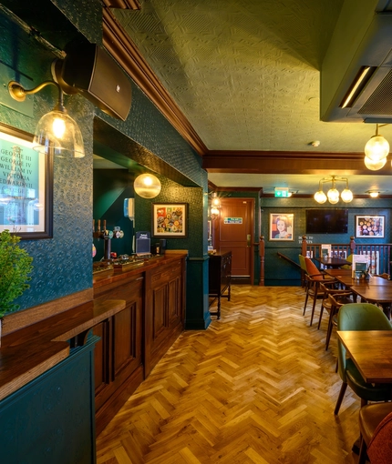 The upper floor wood panelled bar and interior restaurant seating area at The Globe; with parquet flooring, and TVs on the walls.