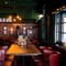 The bar and interior restaurant seating area at the King's Head, with dark wood panelled walls; green velvet curtains; upholstered chairs; and green, textured wallpaper on the ceiling.