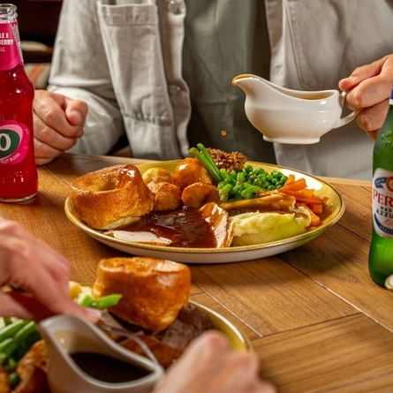 An image of gravy being poured over a Sunday Roast with various drinks within the interior restaurant and seating area at a Hungry Horse venue.