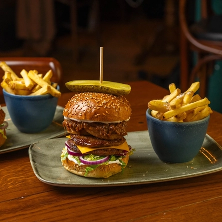 A Chicken Burger and a Pulled Pork Beef Burger, each served on a plate with a bowl of fries, sitting on a wooden restaurant table.