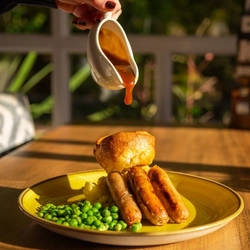 A served main of sausage and mash with a customer pouring gravy available at Hungry Horse venues.