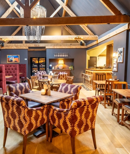 An image of the interior restaurant seating area with wooden beamed vaulted ceiling and tables dressed with floral arrangements at The Black Swan.