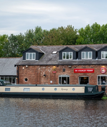 The exterior facade, signage, and waterside at The Stanley Ferry, with canal boats on the water in front of the venue.
