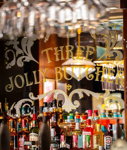The interior bar area focusing on a mirror that says 'Three Jolly Butchers' and has spirits all lining the bottom of it at the Three Jolly Butchers.