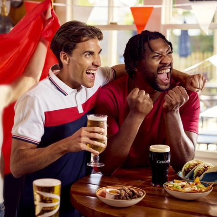 A group of friends sat round a table with drinks and small plates of food enjoying watching a sports event at a Flaming Grill venue.