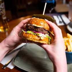 A focused image on a main burger meal served in the restaurant and seating area in a Urban Social venue with another burger meal blurred in the background and drinks served with the meals.