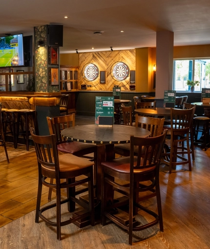 An interior restaurant seating area at the Rudds Arms in Marton-In-Cleveland; with TVs on the walls, and two illuminated dartboards.