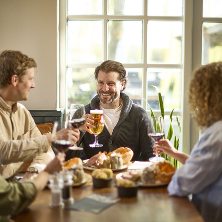 An image showing 4 people sat at a table within the interior restaurant seating area enjoying various food dishes and drinks at a Chef & Brewer venue.