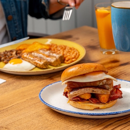 A plated breakfast bap  and Full English Breakfast, on an indoor table.