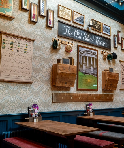 An interior restaurant seating area at the Old School House, with upholstered bench seats, and artwork and photographs on the wall showcasing the history of the venue.