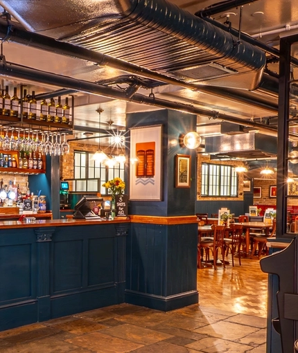 The wood panelled bar inside the Monument in Whitechapel, with stone floor and bottles of wine on shelves above the counter.