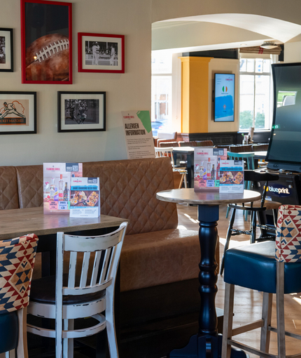 An interior restaurant seating area at Whitehills, with an upholstered booth seat, framed photographs on the wall, and a pub gaming machine.