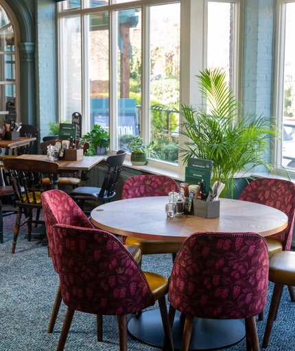 An interior restaurant seating area at the Golden Hind, with upholstered chairs, large windows, and potted plants.