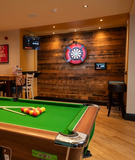 The interior pub gaming area at the Arch & Anchor, with a pool table, dartboard, TVs on the wall, and a restaurant table. 