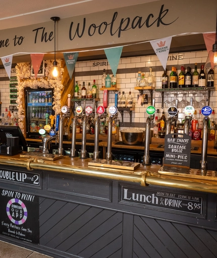 A close up view of the bar inside The Woolpack Inn in Norwich, with golden drinks trays and a gold hand rail on the counter, and bunting hanging overhead.