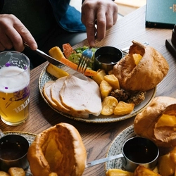A close up image of a person sat at a table within the interior restaurant seating area enjoying a drink and a roast at a Heritage venue.