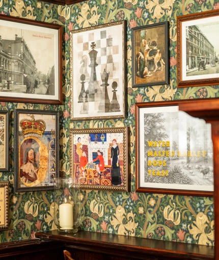 A close up view of framed artwork on a floral wallpapered wall inside the King's Head.