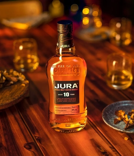 A bottle of Jura whisky and glasses on a table with small plates of sweet treats.