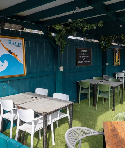 The under cover exterior beer garden seating area at The Victoria in Lytham St Annes, with ivy and string lights on the ceiling and framed artwork on the walls.